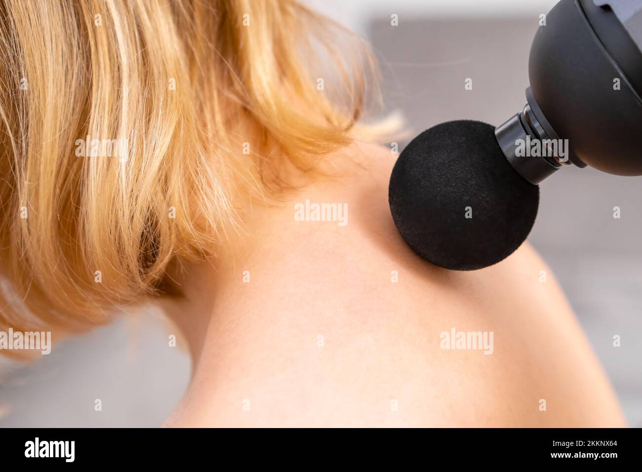 Blonde hair woman massaging a neck using a massage gun. Sport recovery