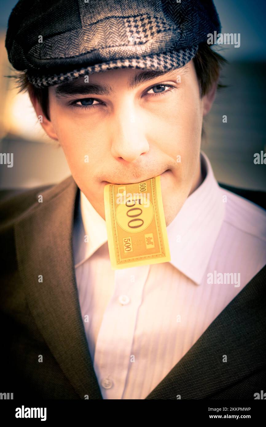 Big Spending Man Eating Away His Cash Earnings When Putting A 500 Dollar Note In His Mouth In A Sign Of Bills, Consumption And Financial Debt Stock Photo