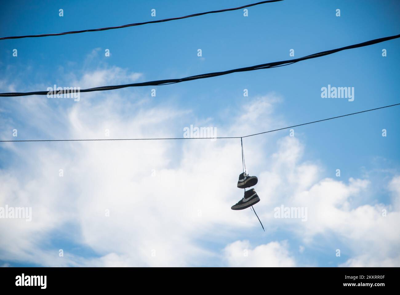 Pair of shoes dangling from telephone wires against blue sky and clouds Stock Photo Alamy