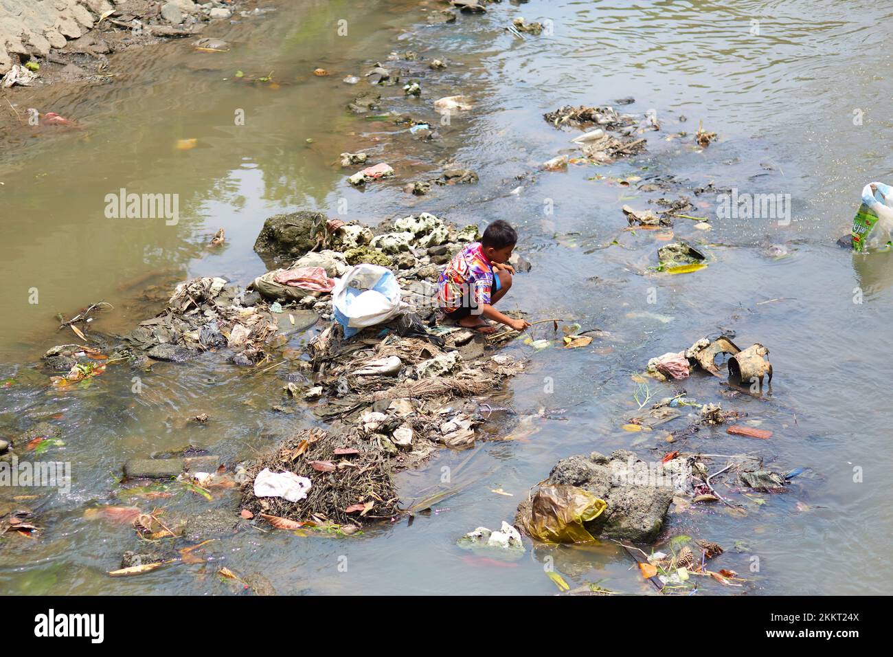 A man digs through the trash floating on the river in search of something of value. Bali, Indonesia - 03.01.2018 Stock Photo