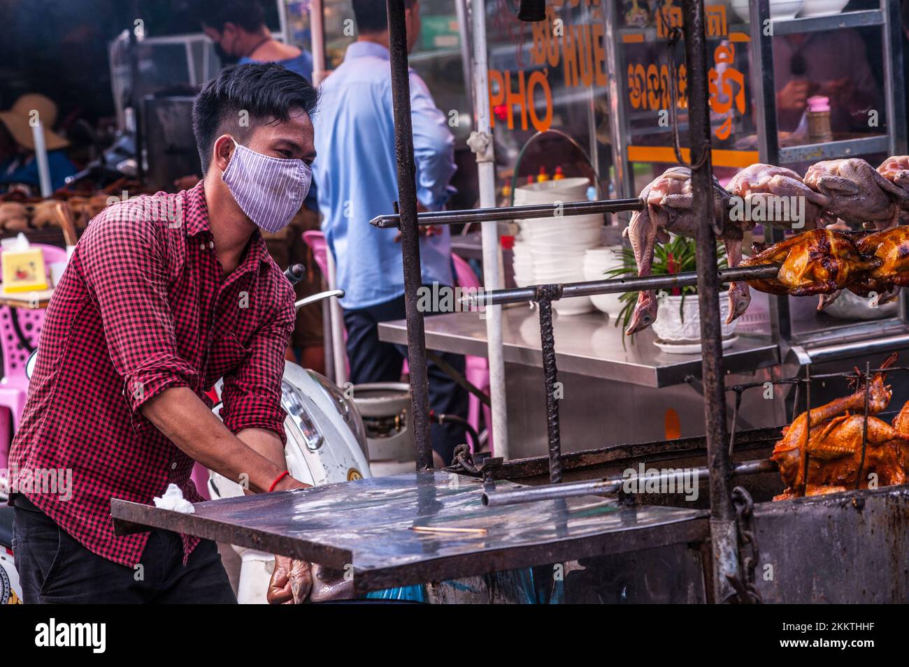 A Cambodian man, wearing a face mask, sells grilled chicken at Kandal Market during the COVID - 19 pandemic. Phnom Penh, Cambodia. © Kraig Lieb Stock Photo