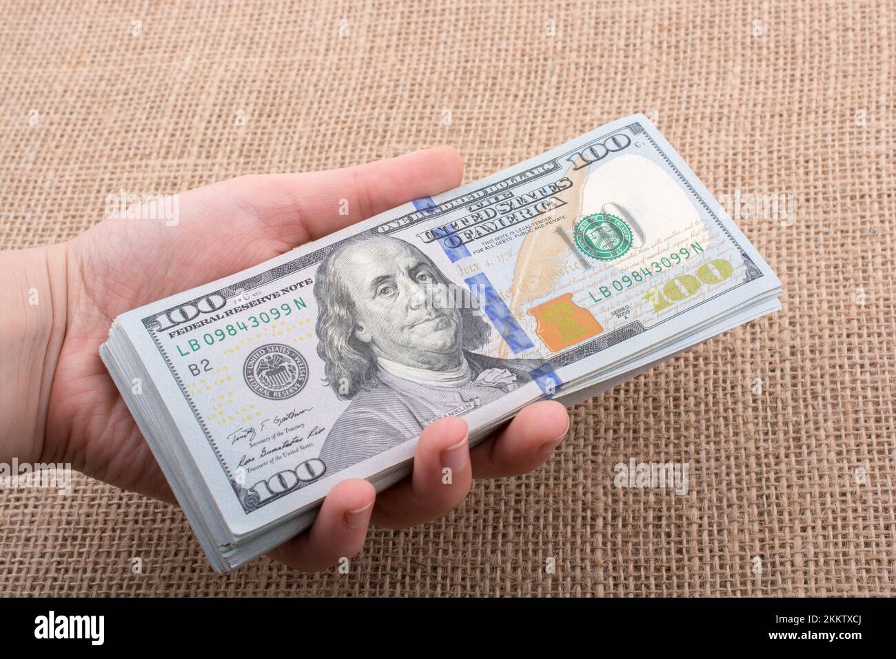 Hand holding banknote bundle of US dollar on a linen canvas background ...