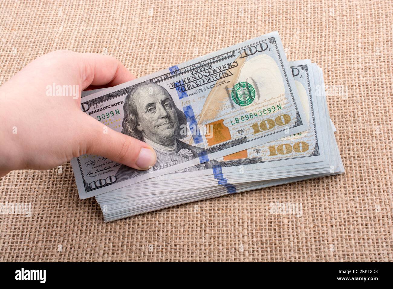 Hand holding banknote bundle of US dollar on a linen canvas background ...