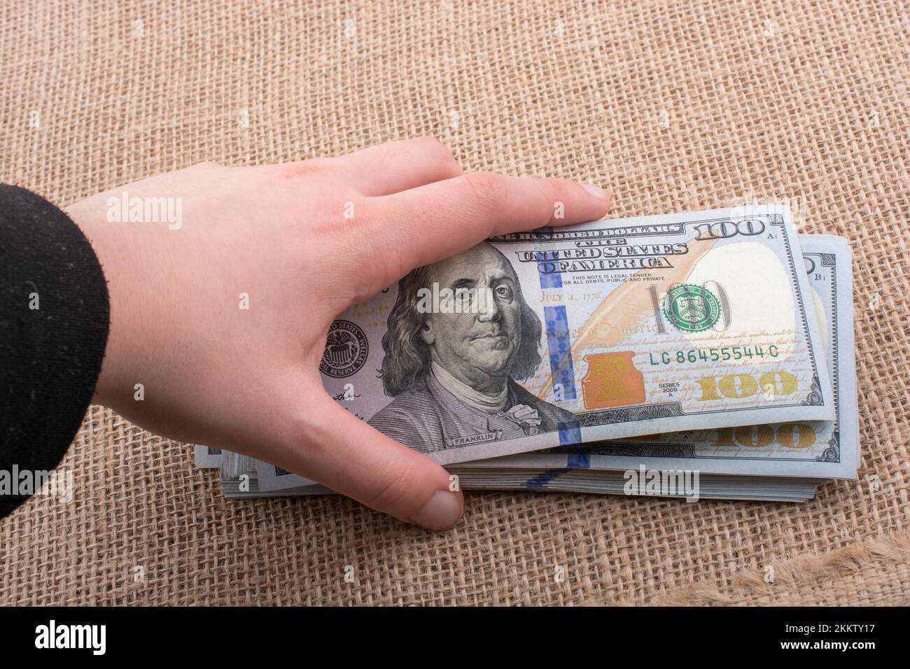 Hand holding banknote bundle of US dollar on a linen canvas background ...