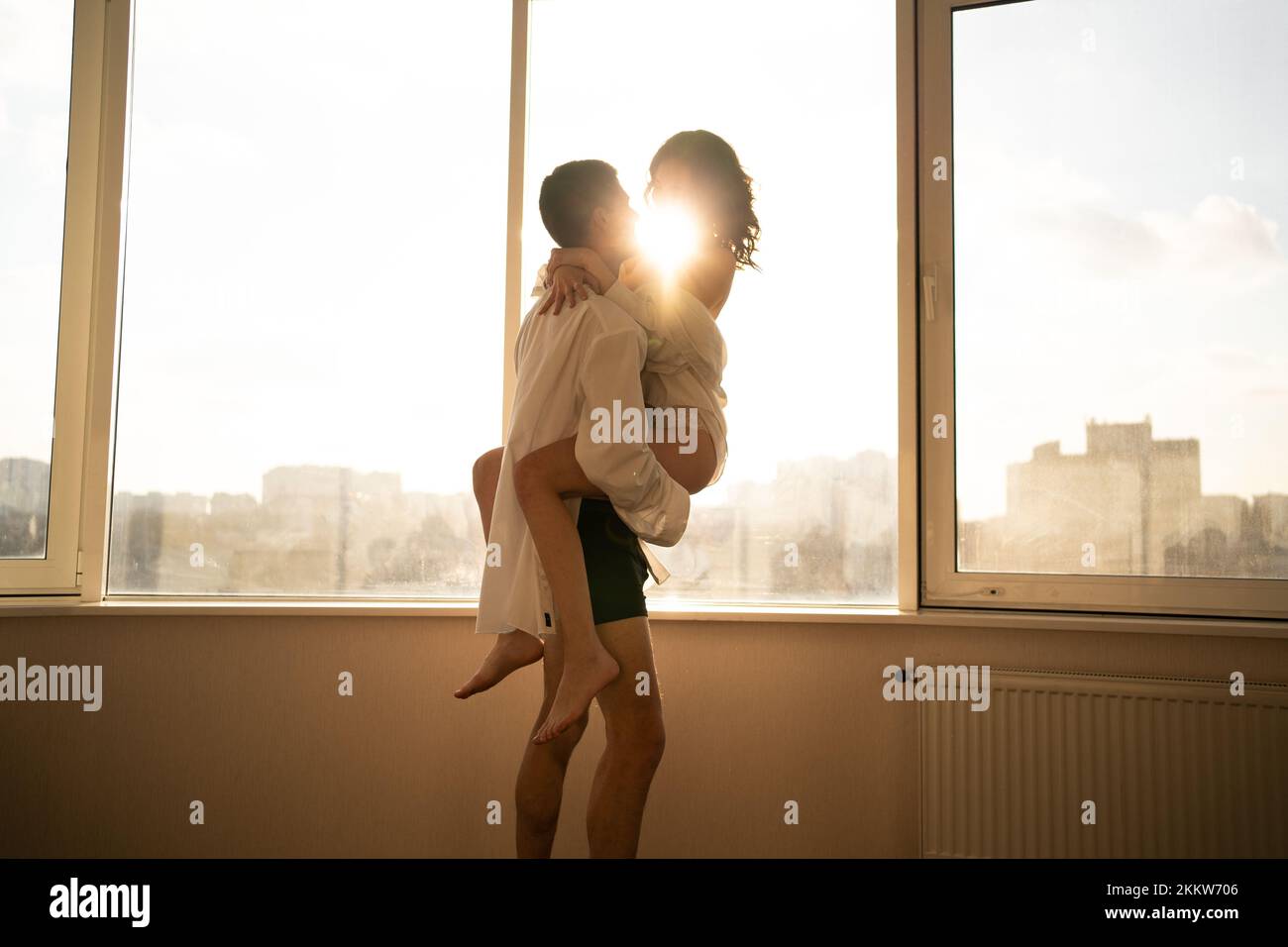 Passion, relationship concept. Happy people, romance, date, fun, white interior. Beautiful couple stand near window embrace, Smile man and woman lover Stock Photo