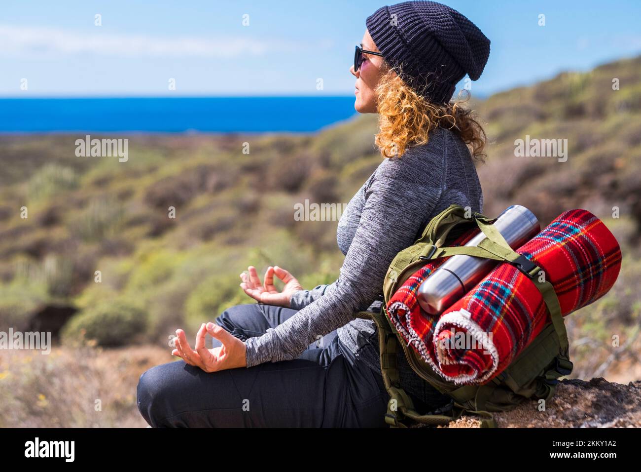 Zen and meditation activity in outdoor leisure lifestyle. Woman with backpack doing lotus position yoga. Concept of alternative healthy lifestyle and Stock Photo