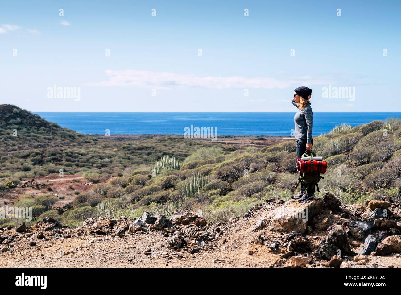 One standing woman enjoying and admiring panorama landscape in outdoor leisure activity after hiking trekking walk. Ocean and sea view with blue sky a Stock Photo