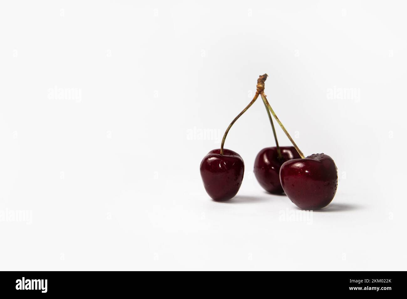 Three red cherries with stems on white background Stock Photo