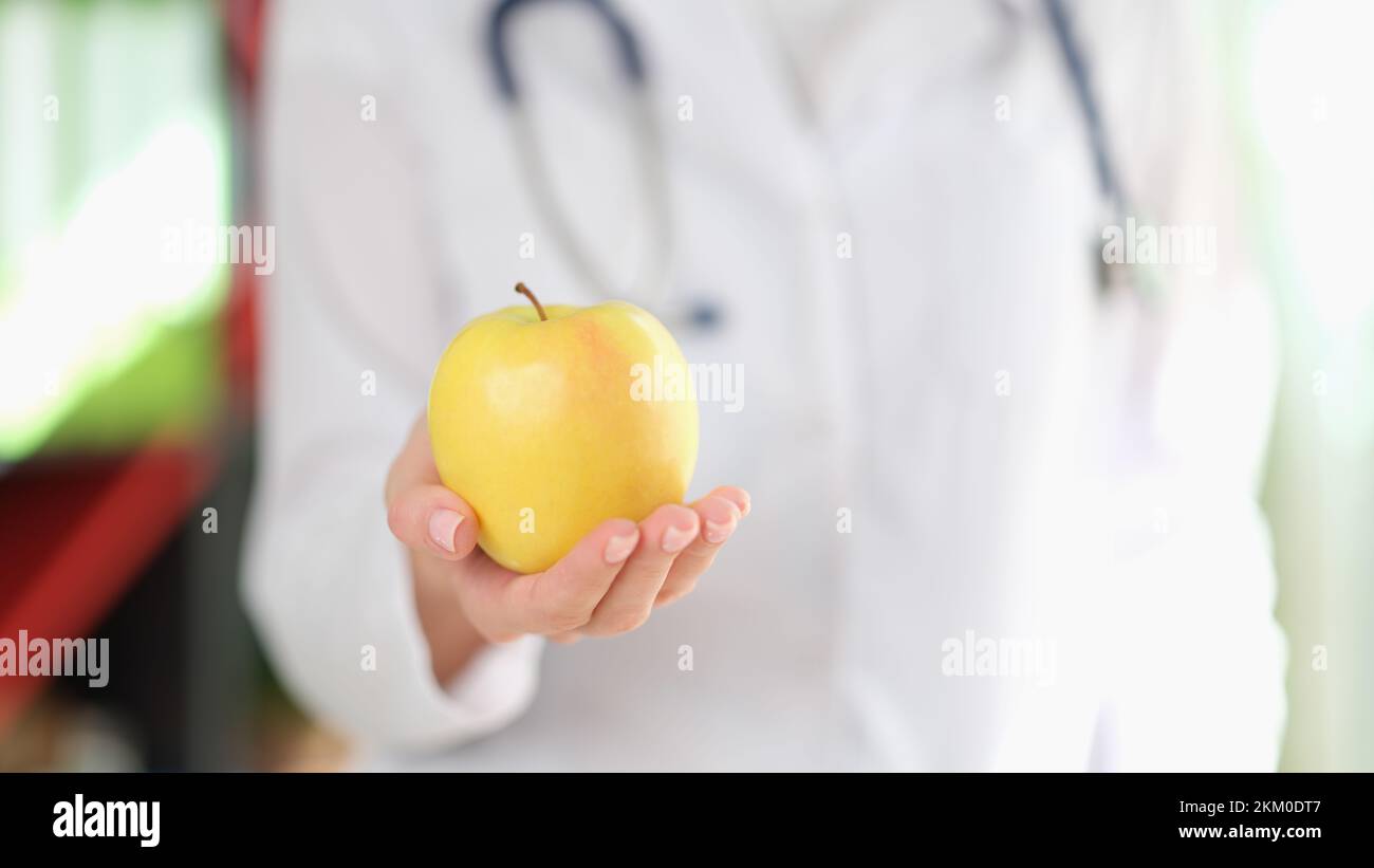 Female doctor nutritionist holding ripe yellow apple in hand Stock Photo