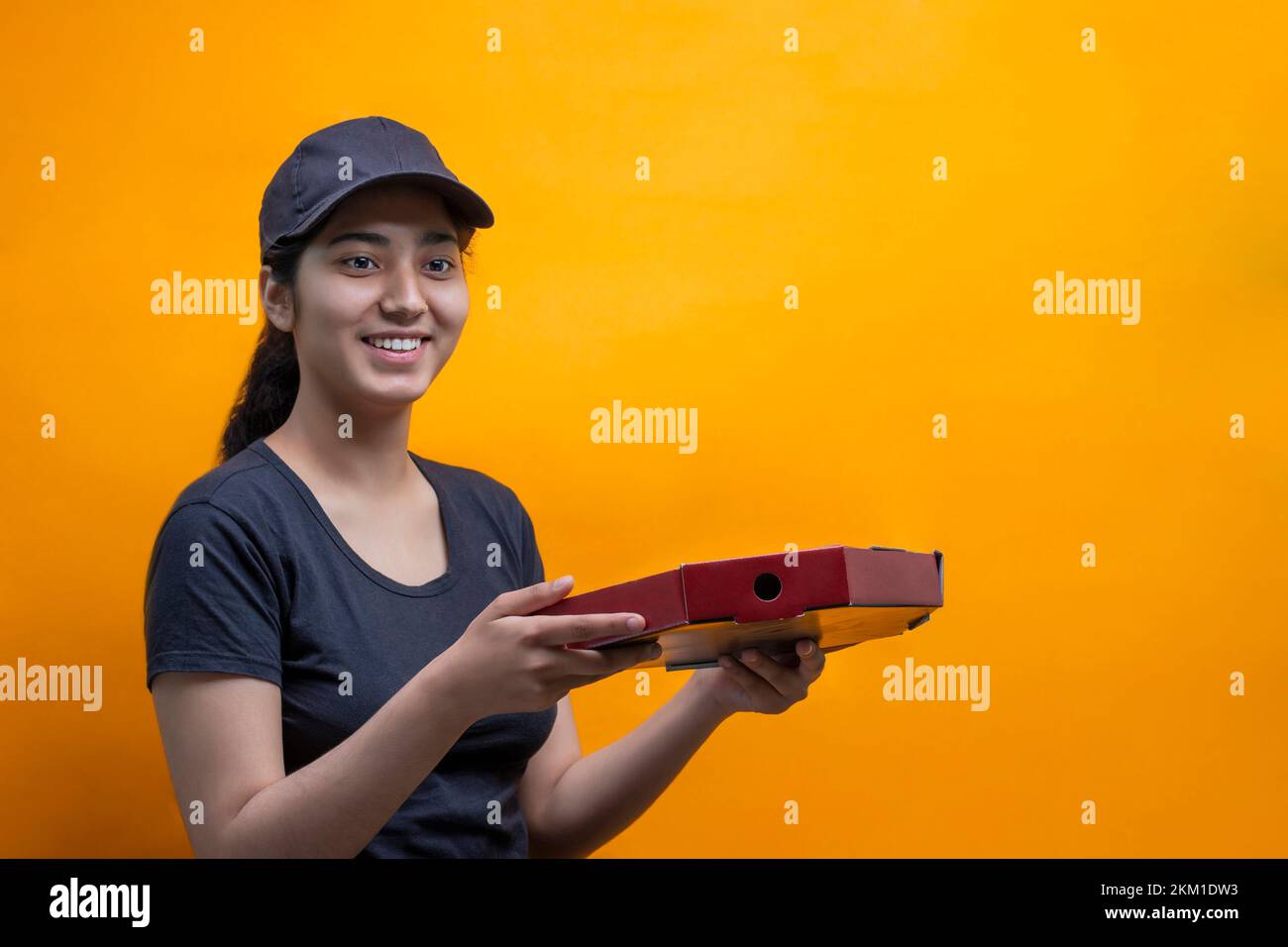 Smiling delivery woman carrying Pizza box against Yellow background Stock Photo