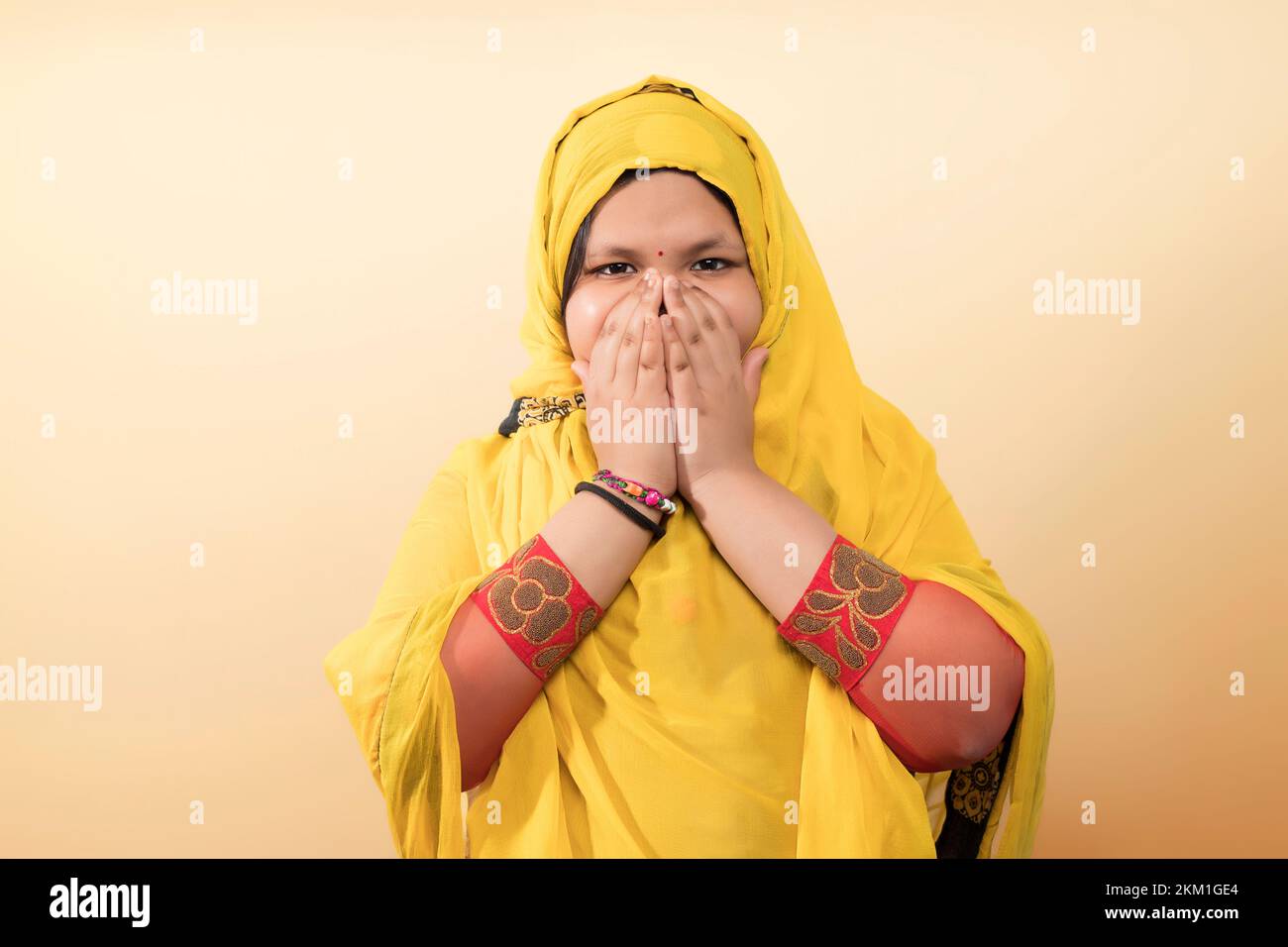 A religious Asian Muslim child girl in the Muslim hijab dress and covering her mouth Stock Photo