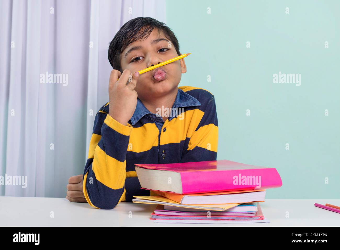 Boy with pencil under his nose over study table at home Stock Photo
