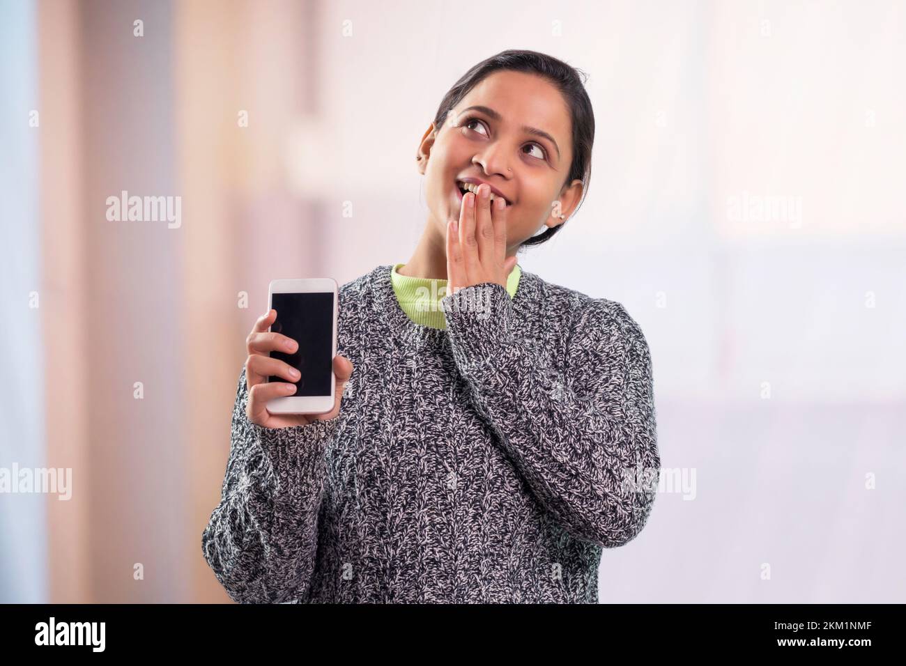 Portrait of young women showing blank screen of mobile phone and covering her mouth Stock Photo