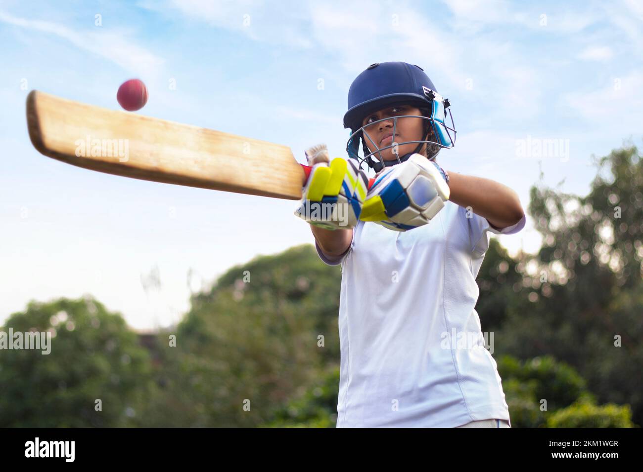 Female cricket player wearing protective gear and hitting the ball with a bat on the field Stock Photo