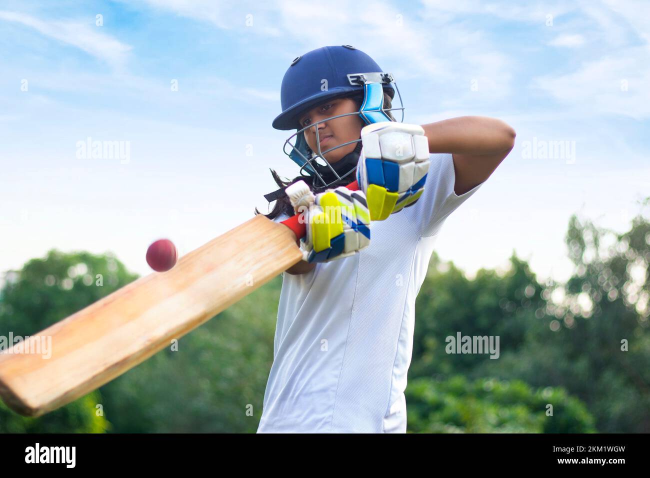 Female cricket player wearing protective gear and hitting the ball with a bat on the field Stock Photo