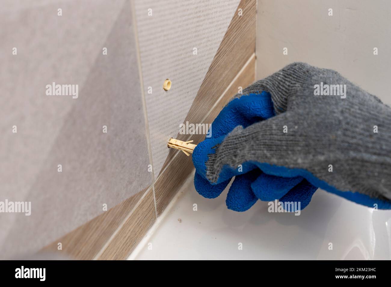 worker's hand inserts a plastic dowel pin into a drilled hole Stock