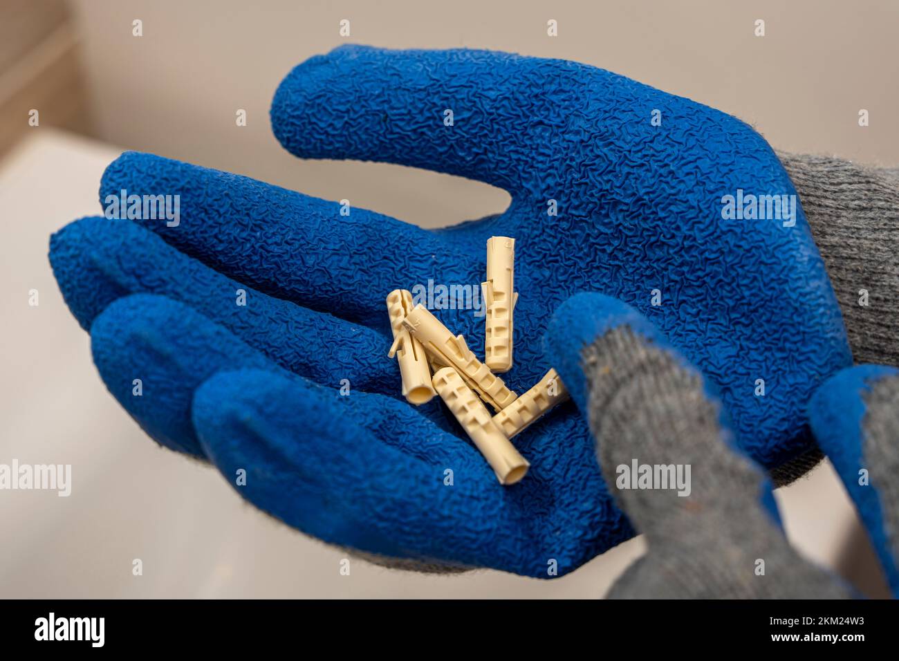 worker's hand in a protective glove holds several plastic dowel pins Stock Photo
