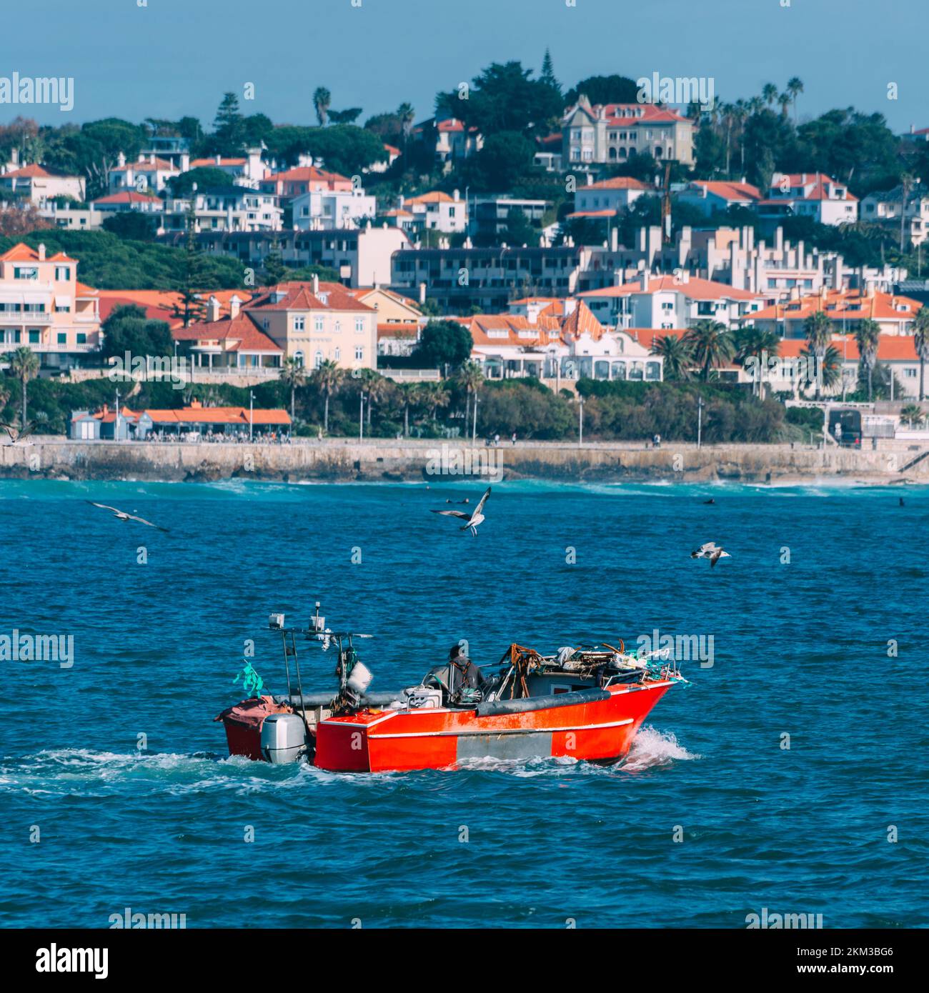 Lone unidentifiable fisherman on a wooden red boat on Estoril Bay in Estoril, Portugal Stock Photo