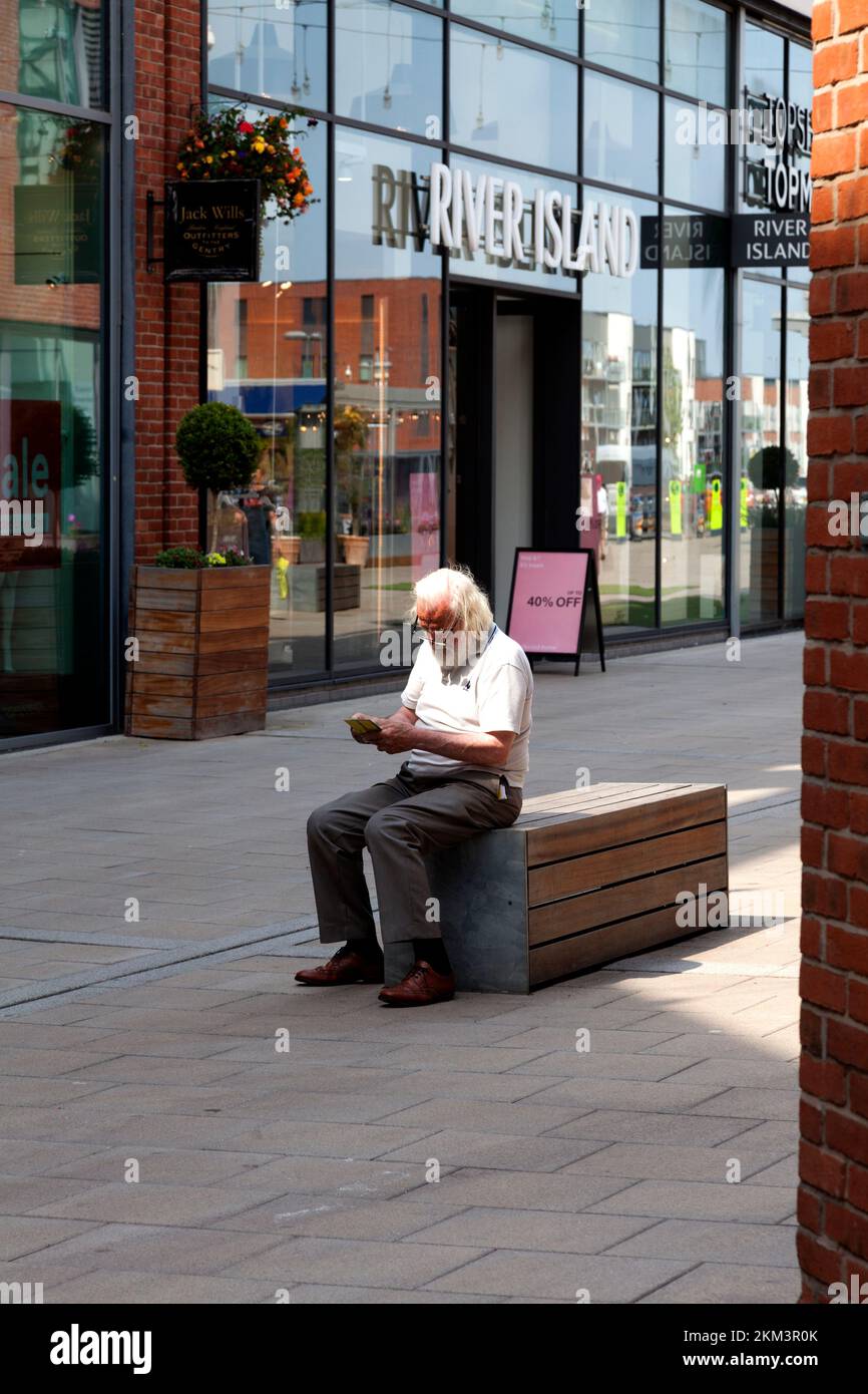Man reading on a bench in the Old Market shopping centre, Hereford, Herefordshire Stock Photo