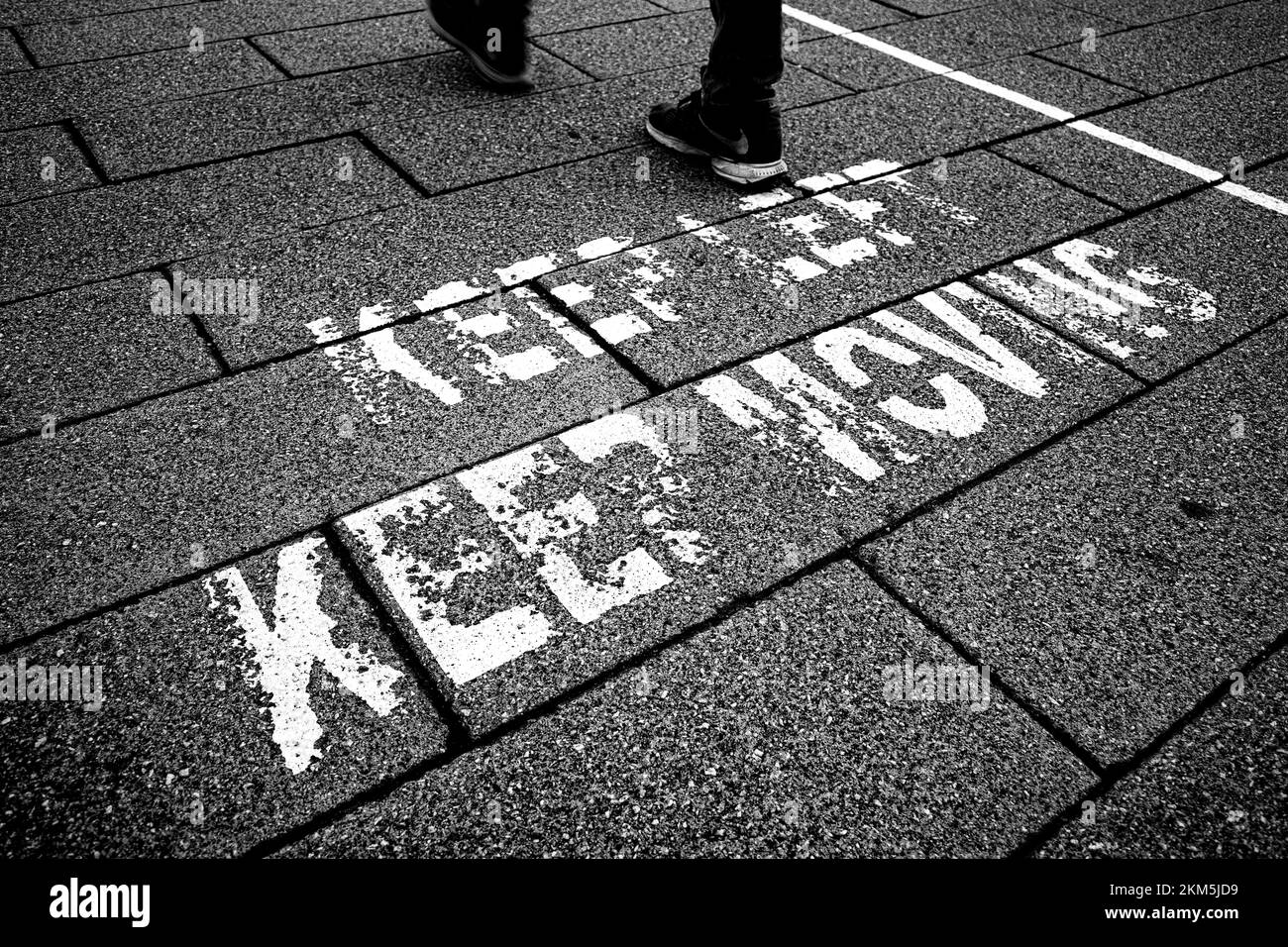 Pavement level view of feet walking. Sign on pavement saying Keep Left, Keep Moving Stock Photo