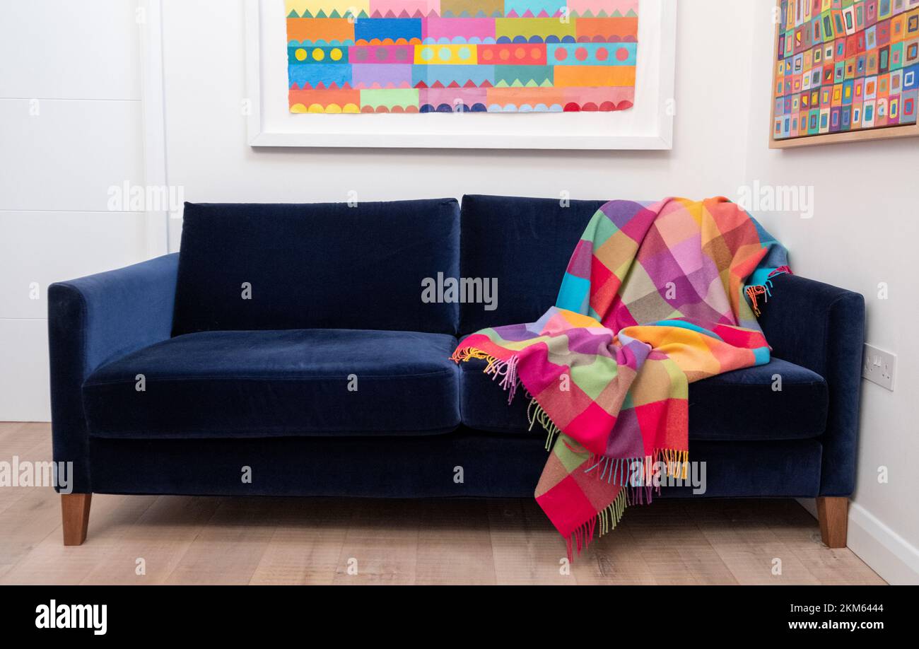 Blue velvet sofa with colourful wool throw blanket, in minimalist
