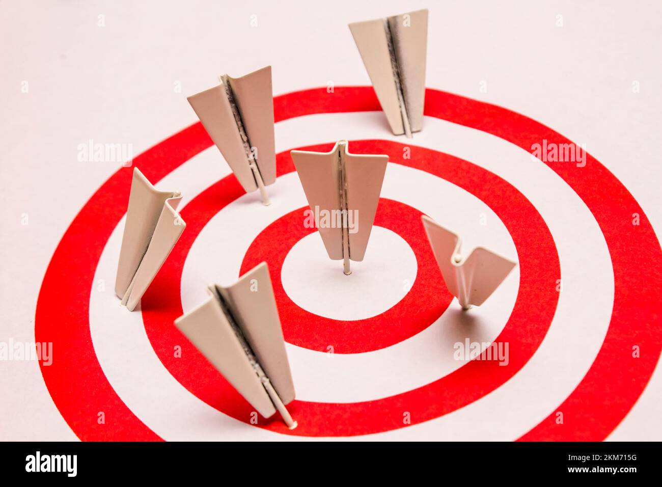 Darts that resemble folded paper airplanes stuck in red and white rings