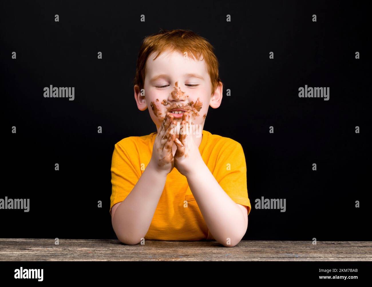the face of a small red-haired boy smeared in milk chocolate, close-up