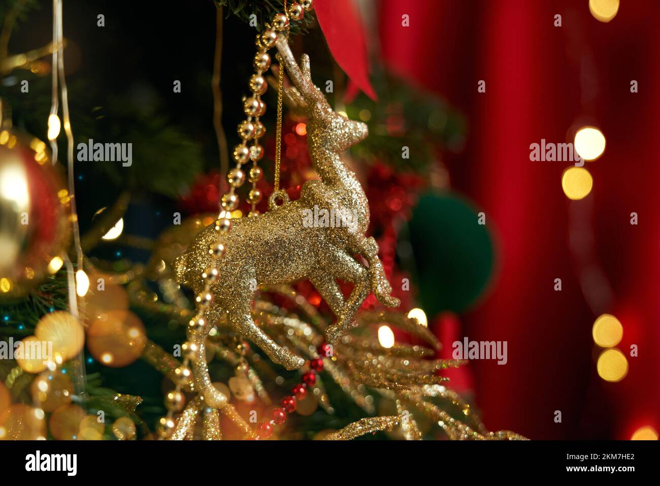 Close up of Christmas tree standing, decorated with golden deer, garlands, balls and bows. People celebrating New Year in cozy decorated room. Concept Stock Photo