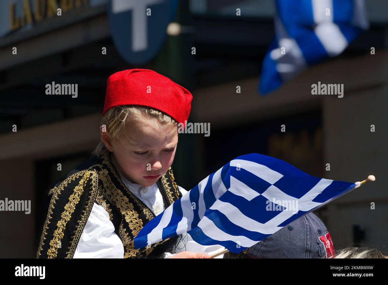 A young child in traditional Greek costume holds a flag on a national holiday, Athens, Greece