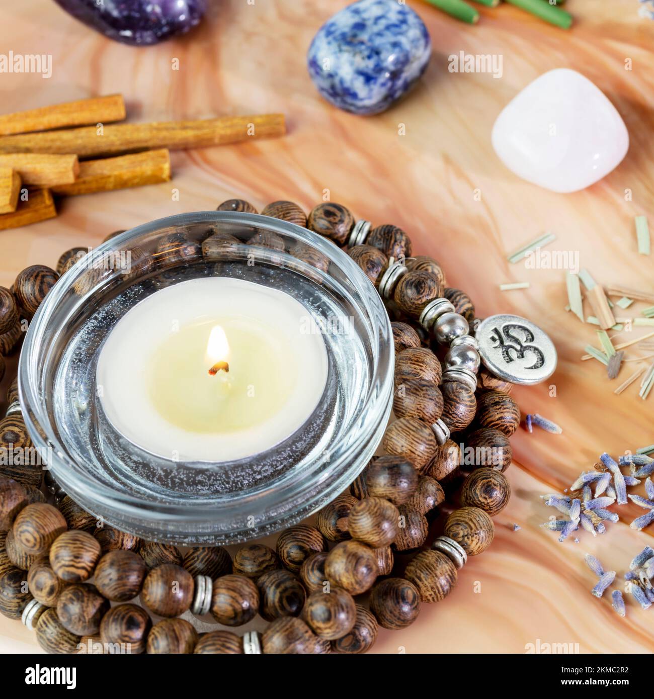 Self-care, healing composition with rosary beads, chakra stones, sandalwood sticks and candle on a pink marble podium. Concept of relaxing at home, en Stock Photo