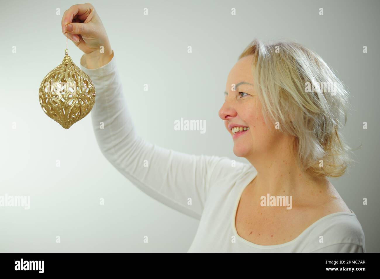 Christmas tree decoration party invitation Adult woman with gray hair with a golden New Year's toy in her hand Beautiful shiny golden ball Stock Photo