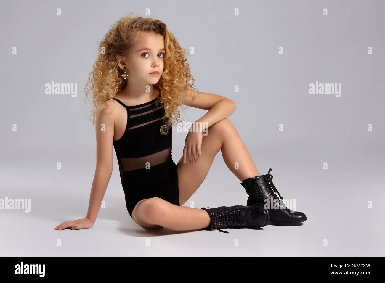 Beautiful little girl gymnast in a black sports swimsuit and boots on a gray background. Stock Photo