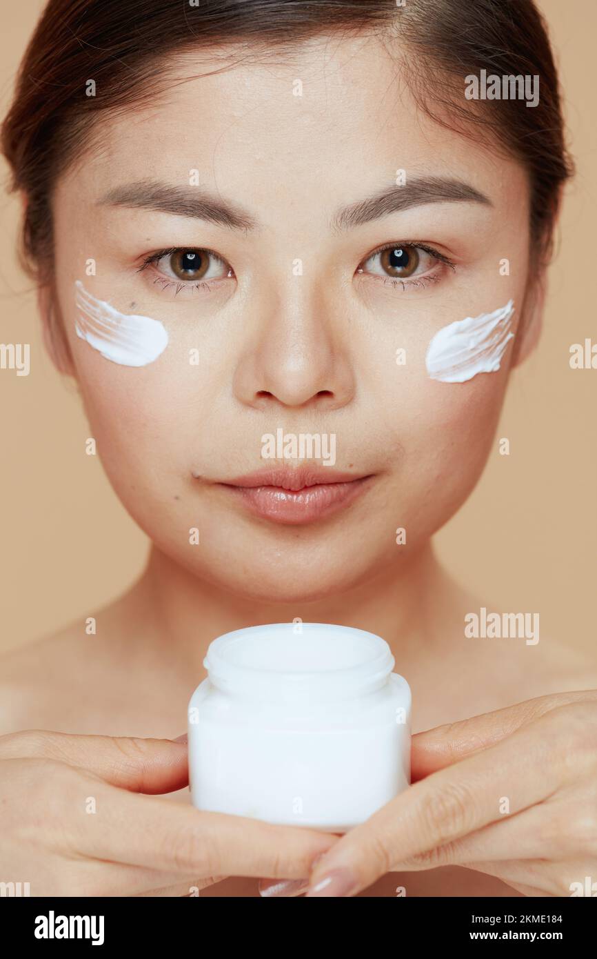 Modern Woman With Facial Cream Jar And Facial Cream On Face On Beige