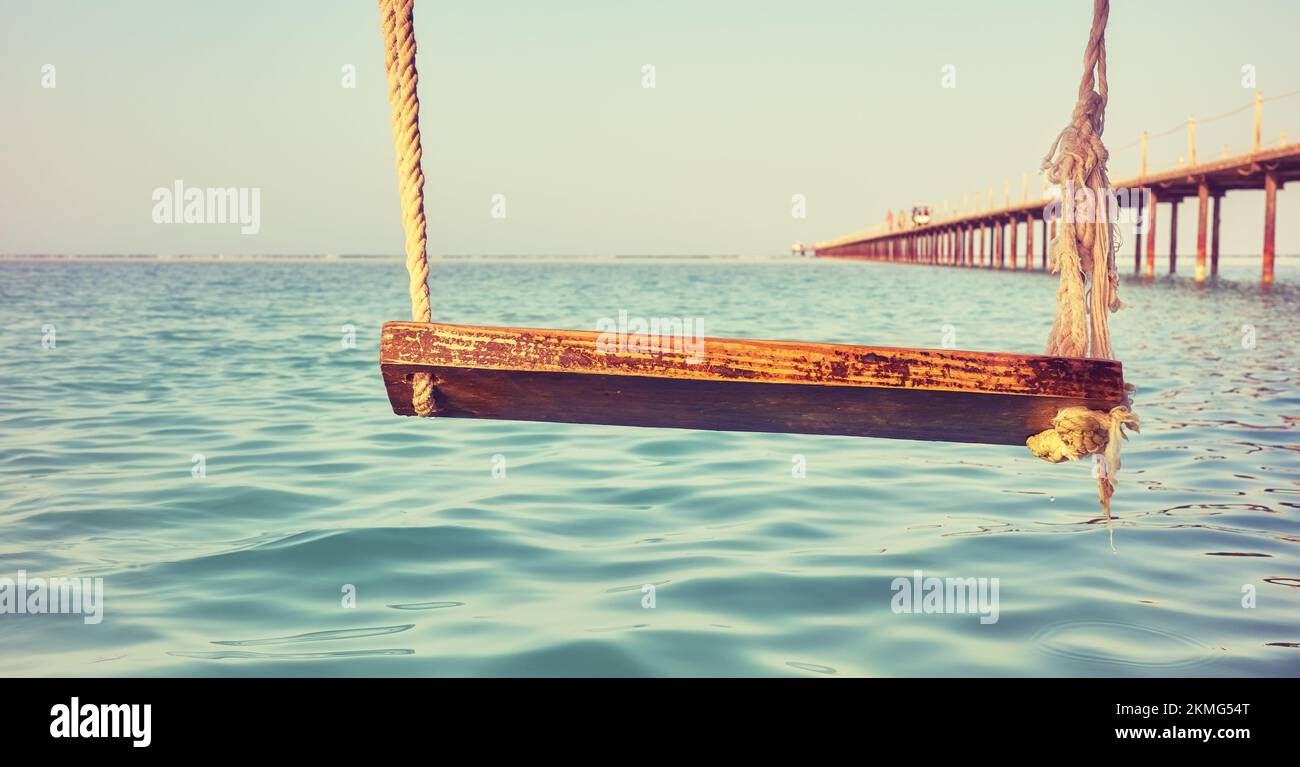 Wooden swing above the water, selective focus, color toning applied. Stock Photo