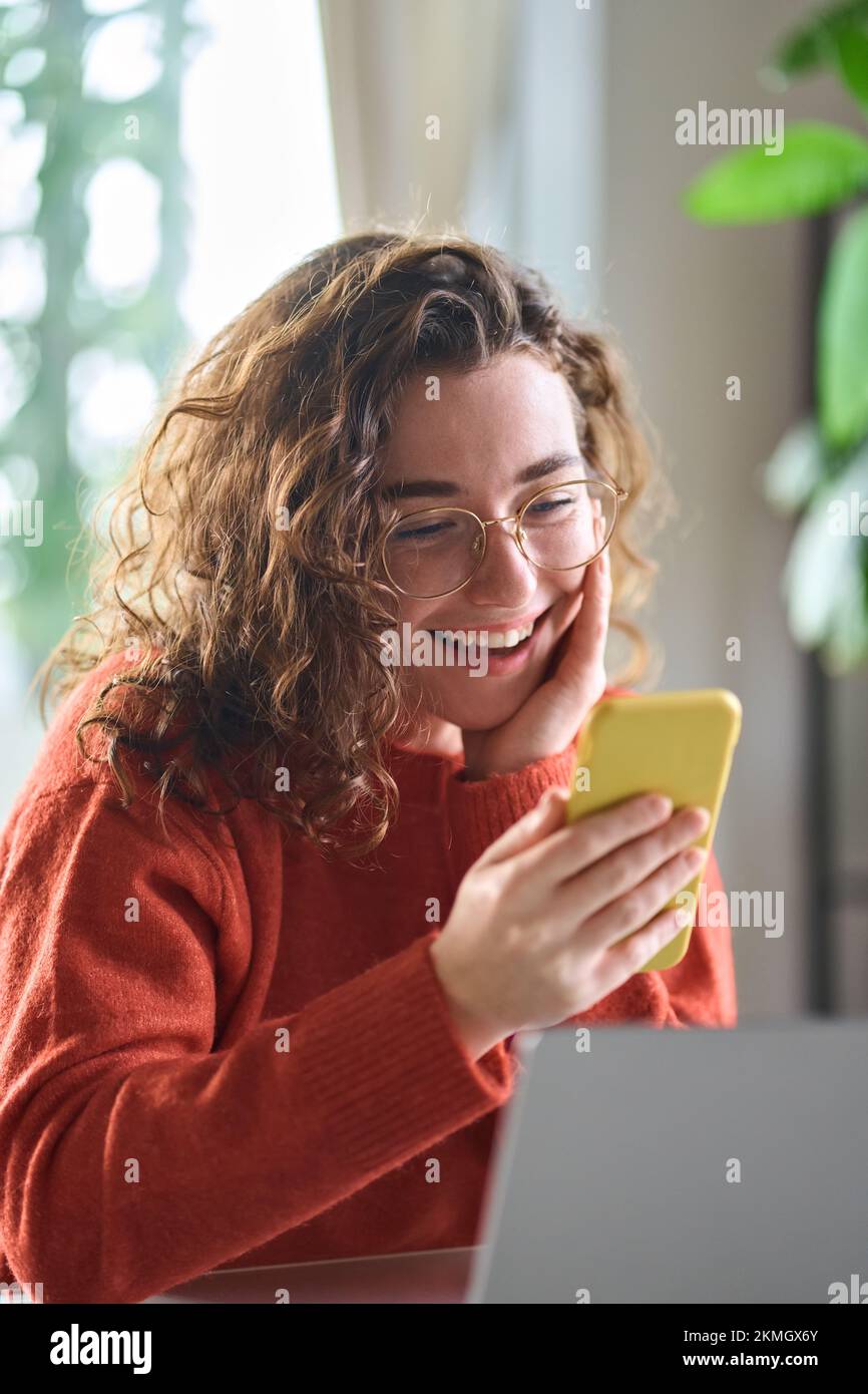 Young smiling lady holding smartphone using cellphone sitting at table. Stock Photo