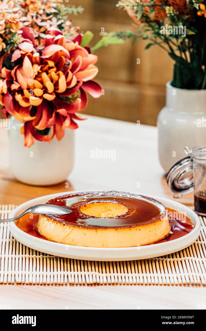 Round caramel flan pudding on a white plate over a wood table with red