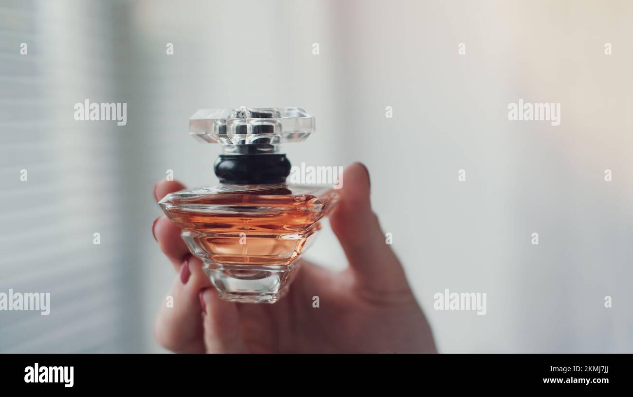Perfume bottle in a female hand against the background of light room