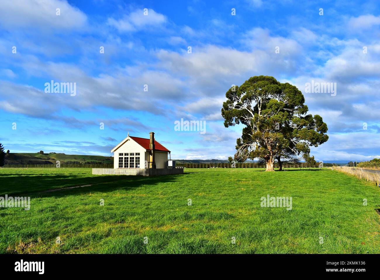 historic schoolhouse amongst field and large tree. Stock Photo