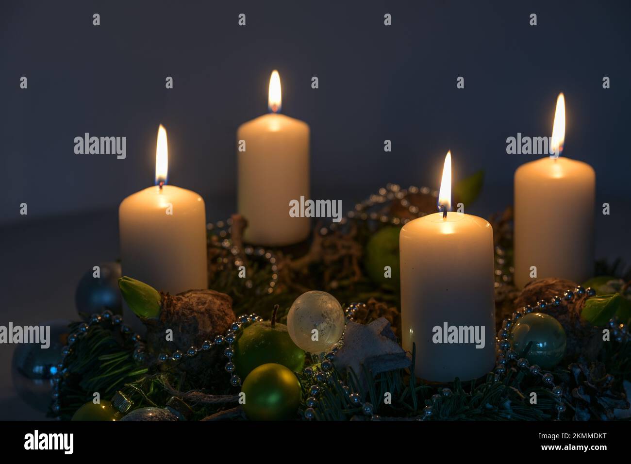 Four white Advent candles on a wreath with Christmas decoration against a dark blue background copy space, selected focus, narrow depth of field Stock Photo