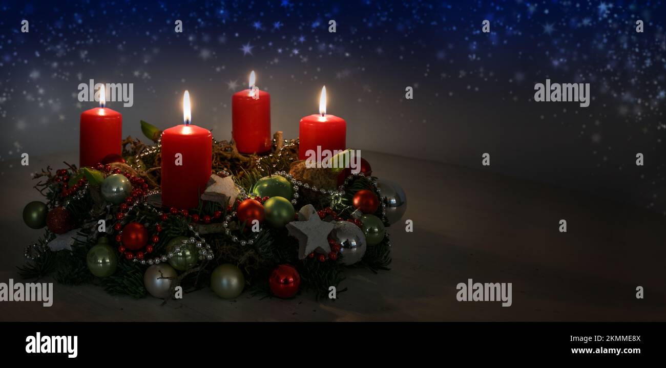Advent wreath with red burning candles and Christmas decoration against a dark blue background