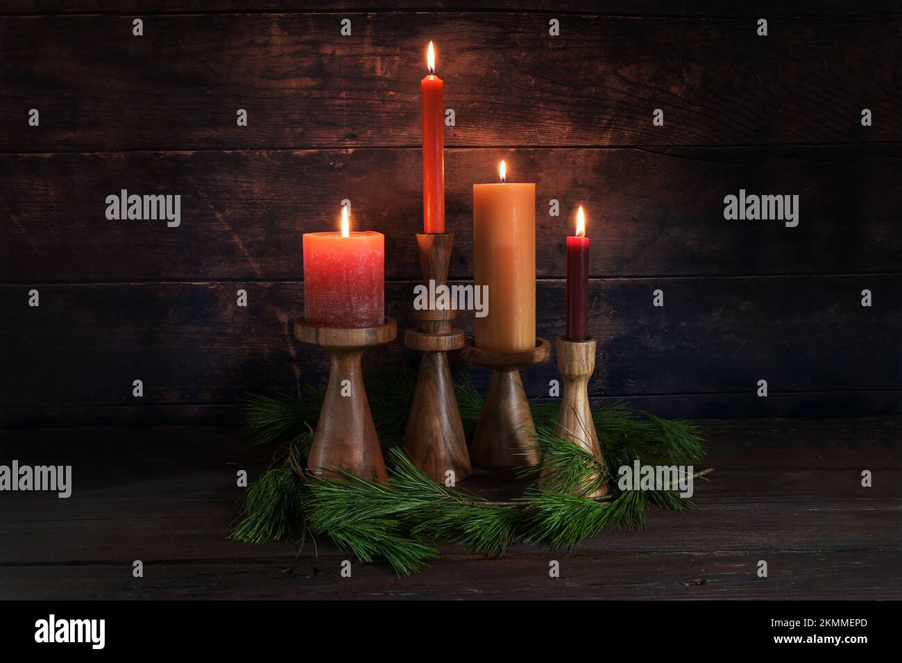 Four different candles in warm colors on wooden stands for Advent with some pine branches against a dark rustic background of wood, copy space, select Stock Photo