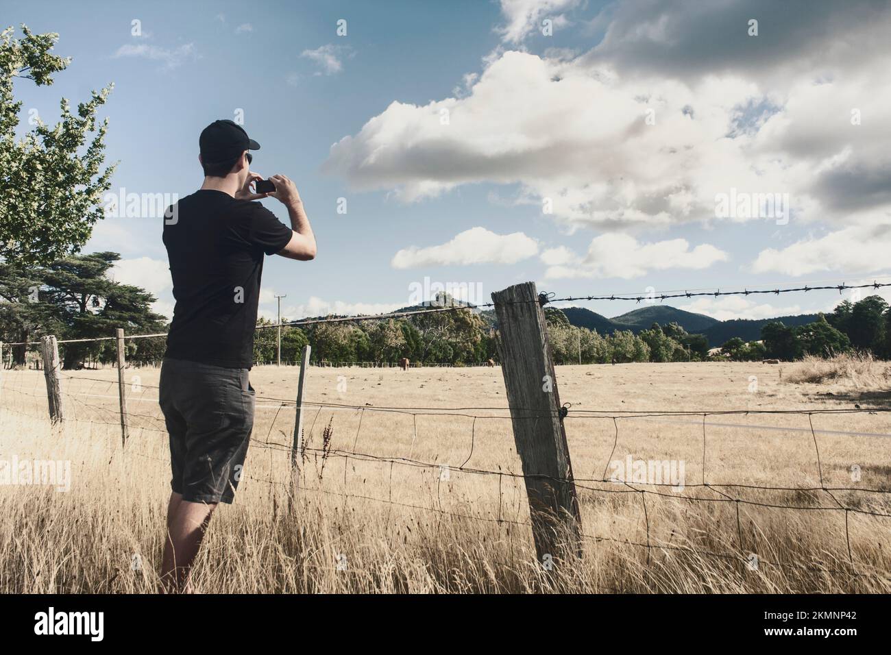 Washed out color photograph of a travelling person in mid 20s taking photograph of a morning meadow landscape on a beautiful cloudy day. Hobart, Tasma Stock Photo