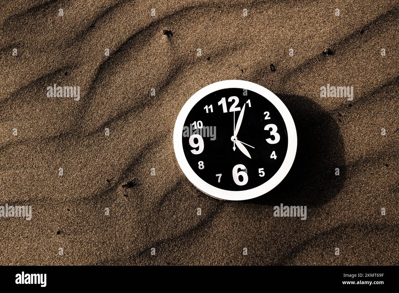 Object photo of a clock stuck in time laying on the surface of dark sand. Clocks and ripples