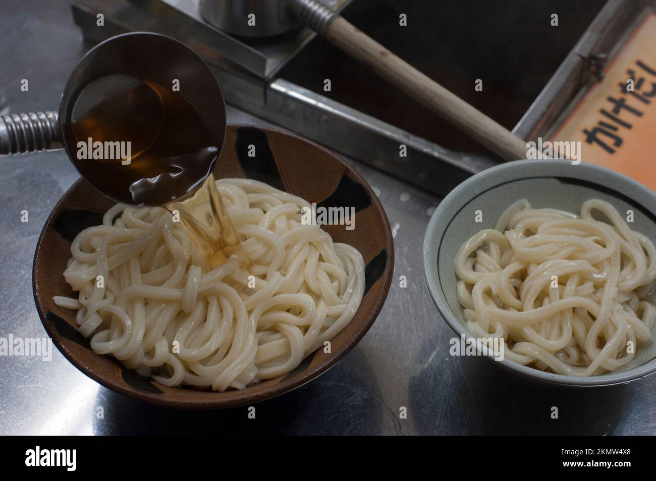 Ladling broth over bowls of chewy udon noodles at Chikusei Udon