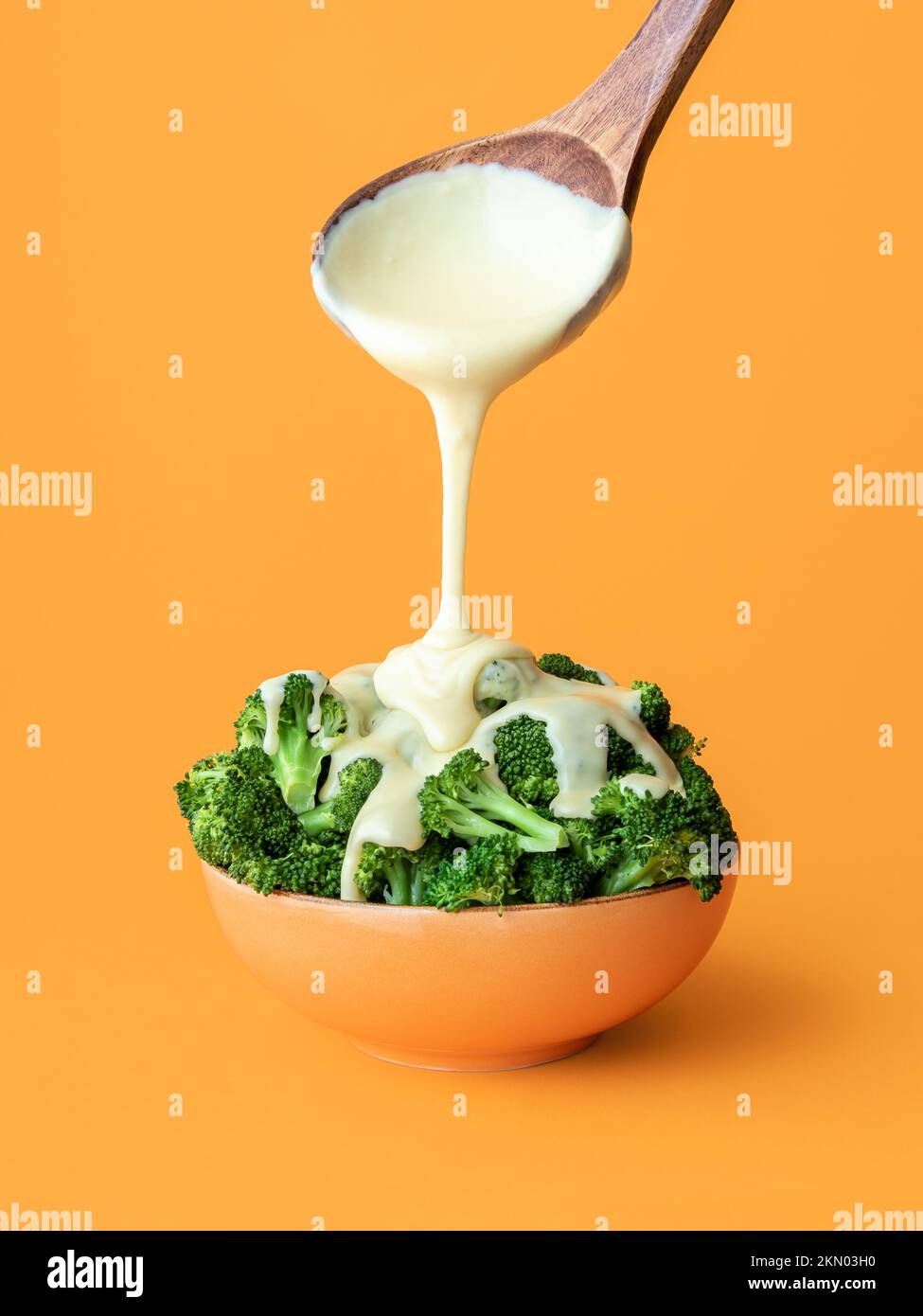 Pouring white cheddar sauce over cooked broccoli, minimalist on an orange background. Bowl with boiled broccoli and delicious cheddar cheese on a colo Stock Photo