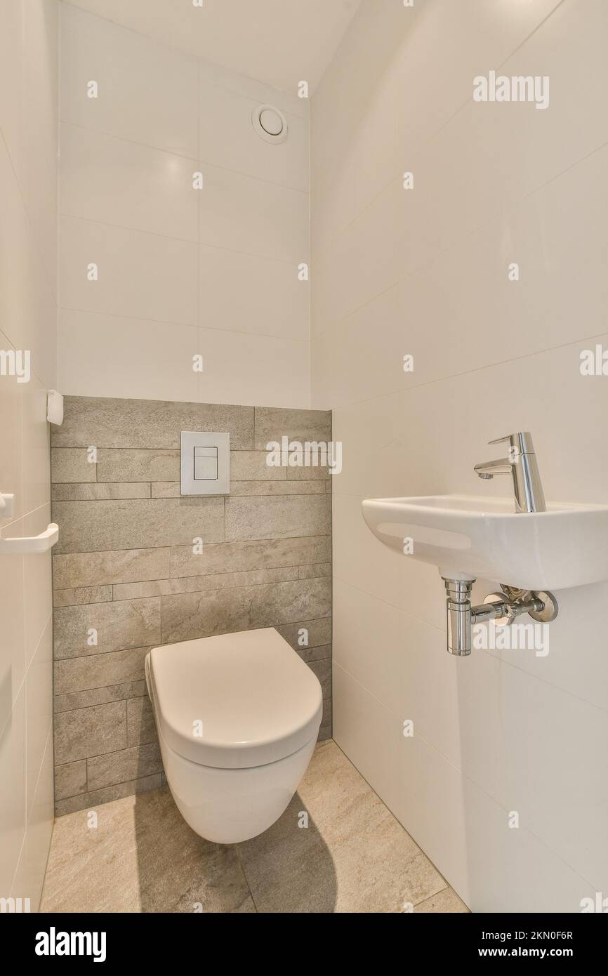 Interior of narrow restroom with sink and wall hung toilet with white