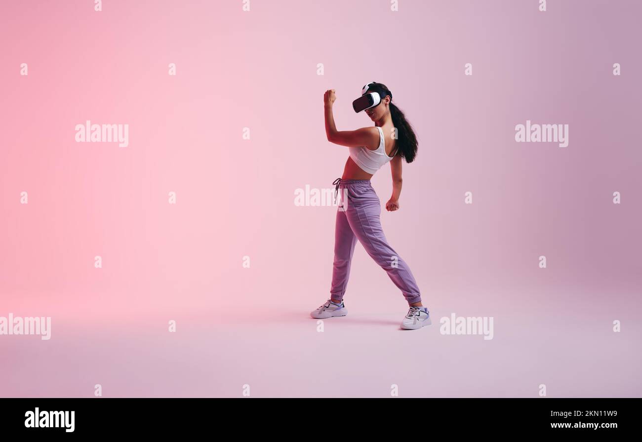 Female gamer exploring a virtual reality game in a studio. Active young woman having fun with virtual reality goggles. Energetic young woman enjoying Stock Photo