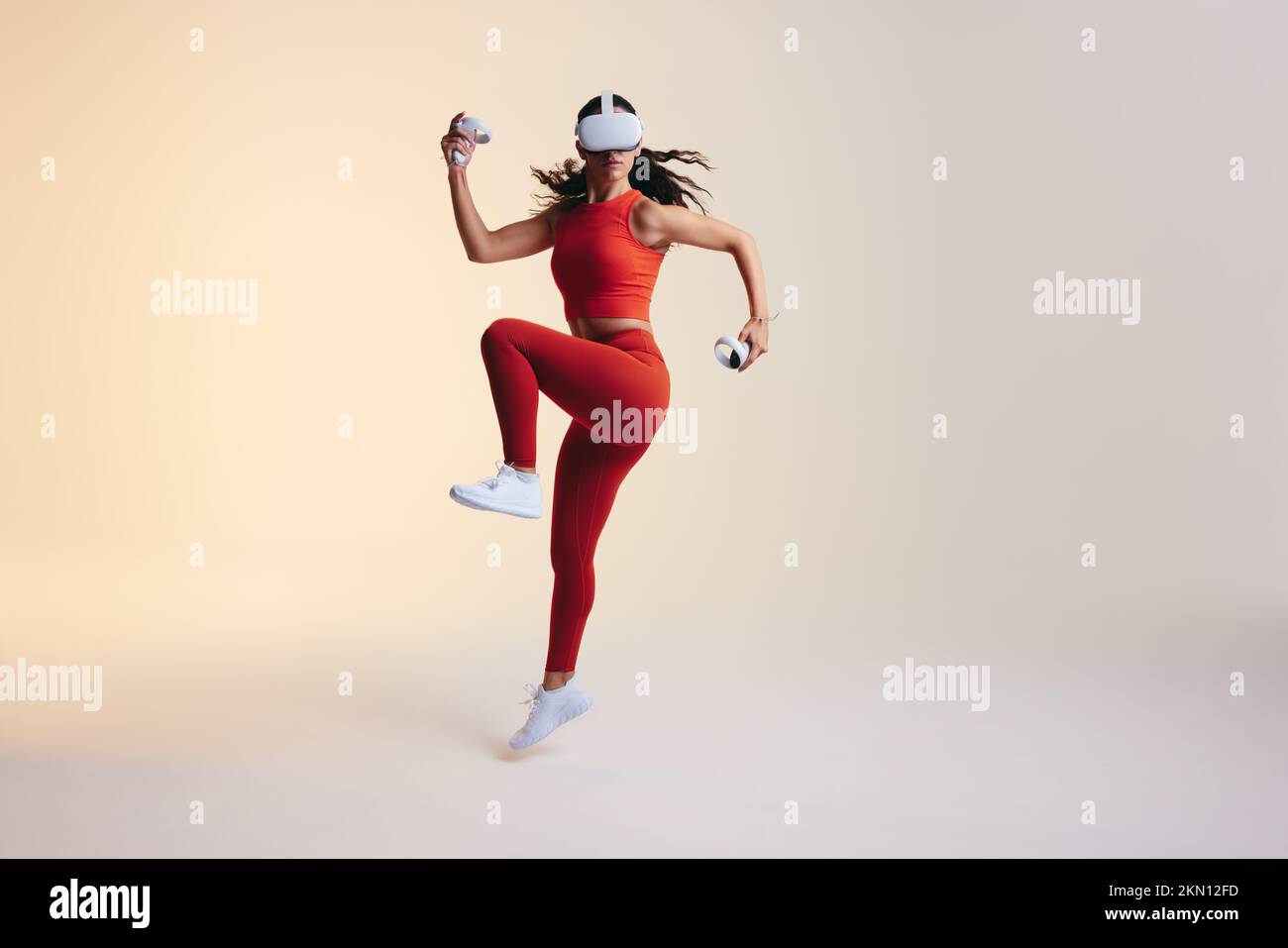 Active sportswoman doing workout moves in virtual reality. Sporty young woman jumping mid air while playing a virtual fitness game. Athletic young wom Stock Photo