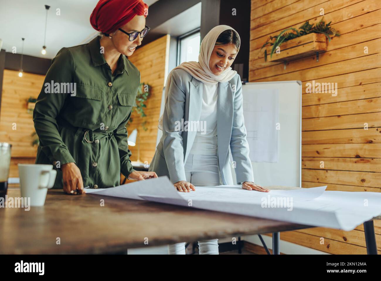 Creative female architects working on blueprint drawings in a modern office. Two Muslim businesswomen planning a new innovative project. Two designers Stock Photo