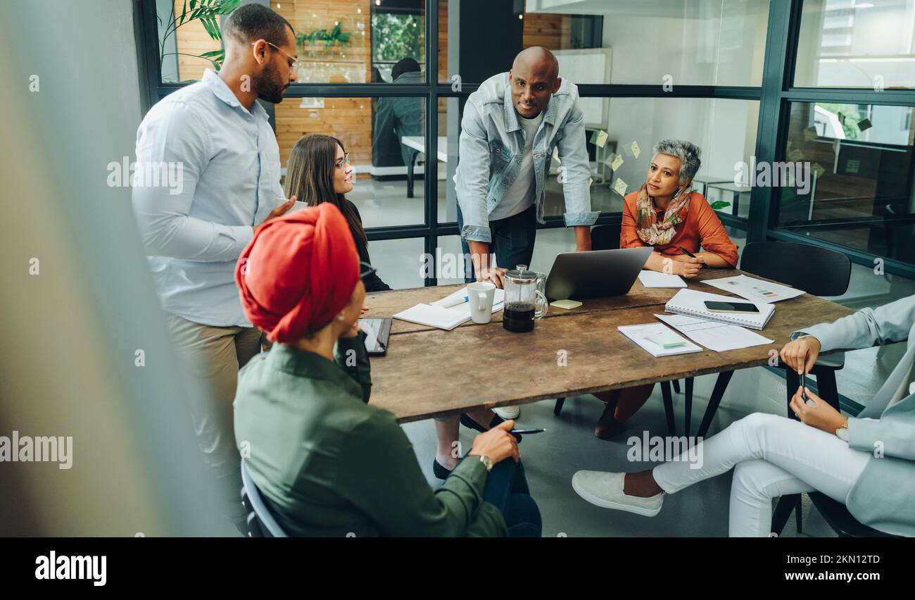 Businesspeople having a group discussion during a meeting in a creative office. Team of multicultural business professionals sharing ideas in an inclu Stock Photo